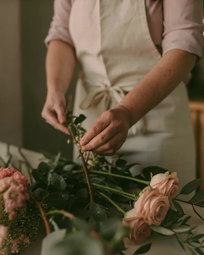Hands arranging pink roses and greenery